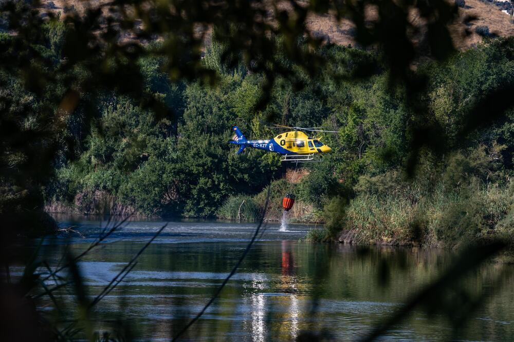 Un helicóptero del Infocam recoge agua en el Tajo para apagar el incendio en una de las islas que el río forma a su paso por Toledo.