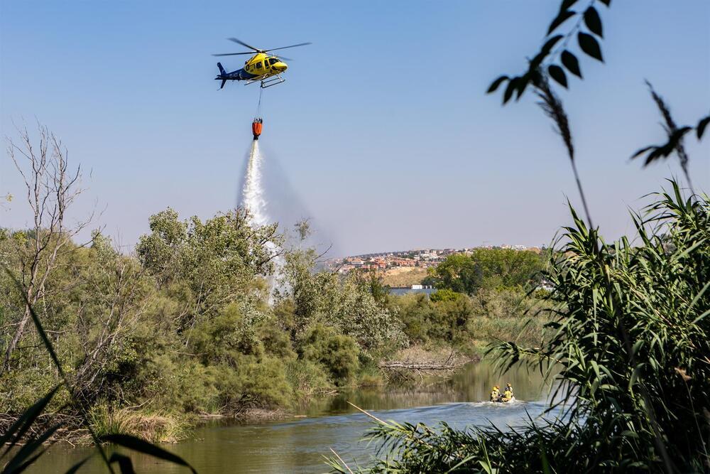 El helicóptero deja caer agua sobre el fuego declarado anoche en una de las islas del Tajo.